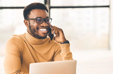 Man smiling and talking on a phone using a laptop