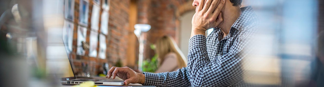 Man researching on laptop at desk, resting his head in his hand