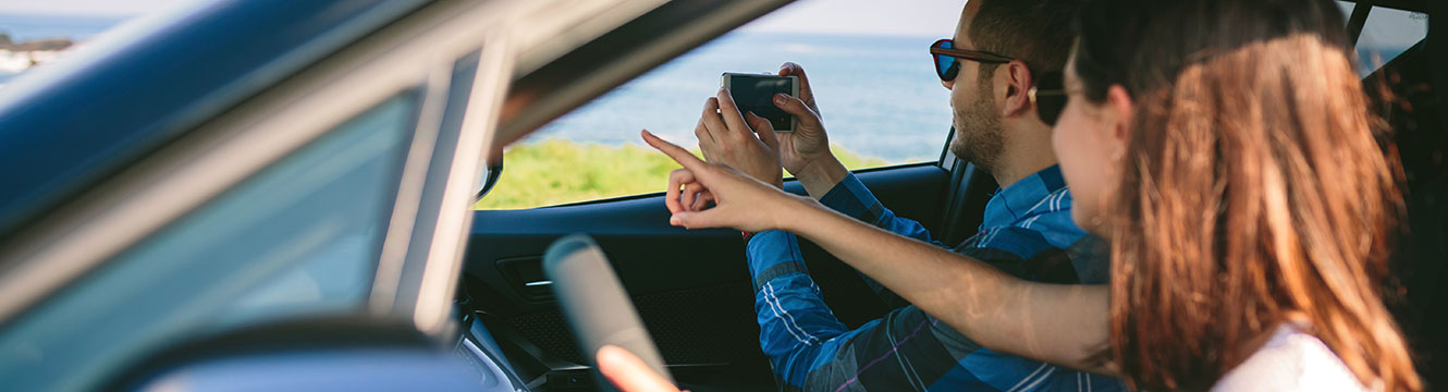 Young couple looking out passenger side car window, woman pointing and man taking photo