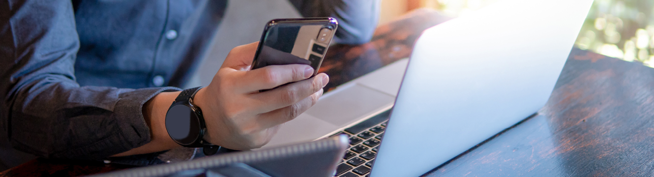 Closeup of a man using a cell phone and working on a laptop