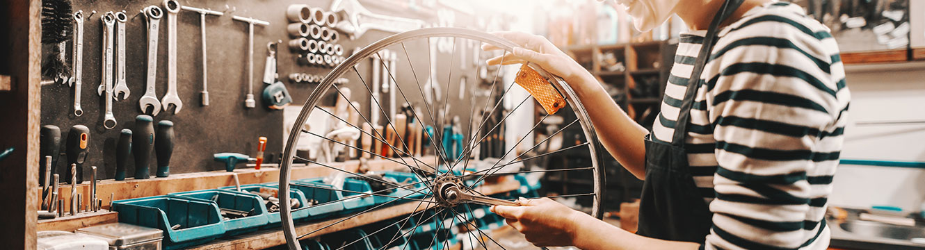 person with an apron on fixing a bicycle wheel on a tool bench