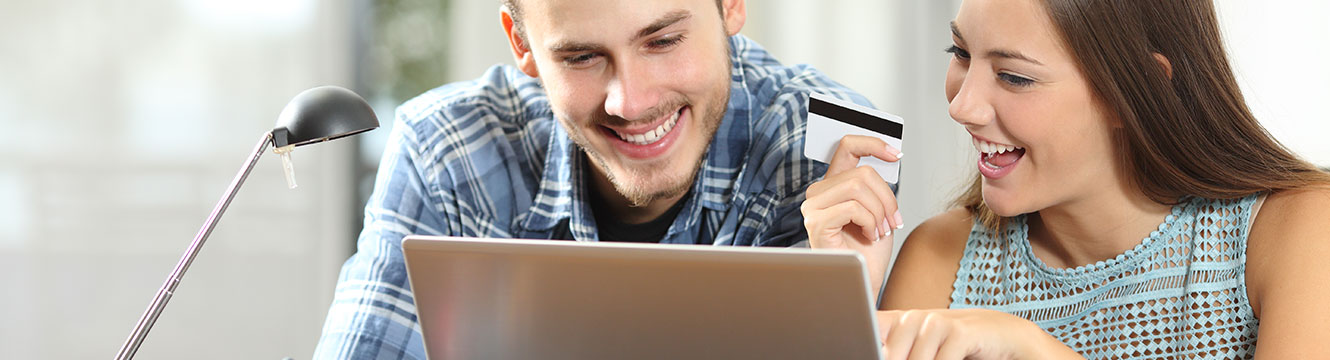 Male and female in their mid-20s smiling at computer while female holds credit card in her hand