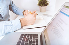 Person writing in a notebook next to an open laptop