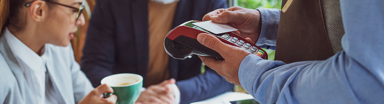 Waiter taking credit card payment on small handheld device at table with man holding a coffee cup